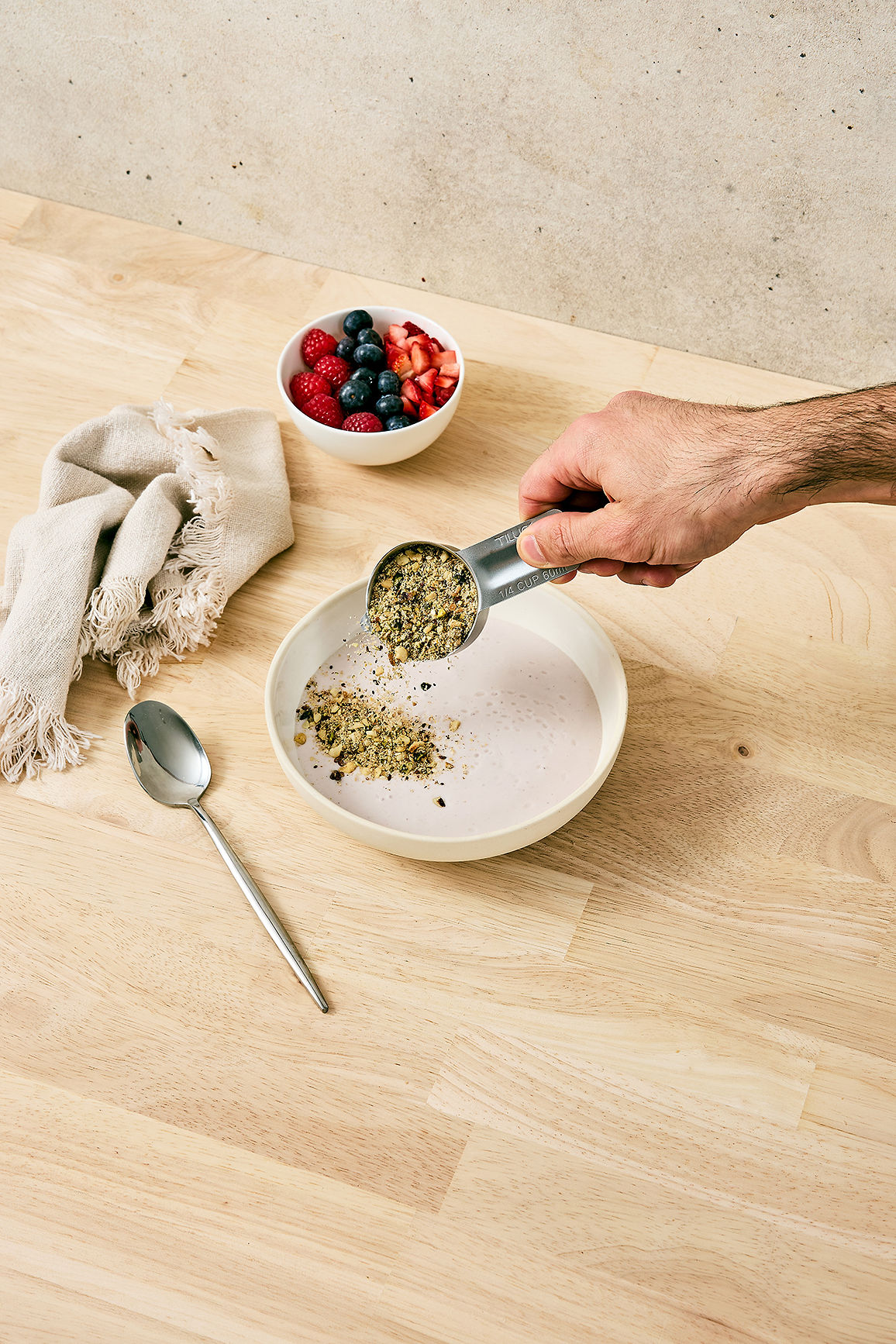 A ¼-cup scoop of My Daily Gut Digestion Blend being poured into a bowl of yoghurt, with seasonal fruit on the side